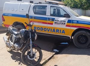 Polícia Militar captura motociclista fugitivo após perseguição por estrada de terra em área rural. Moto e viatura aparecem na imagem.